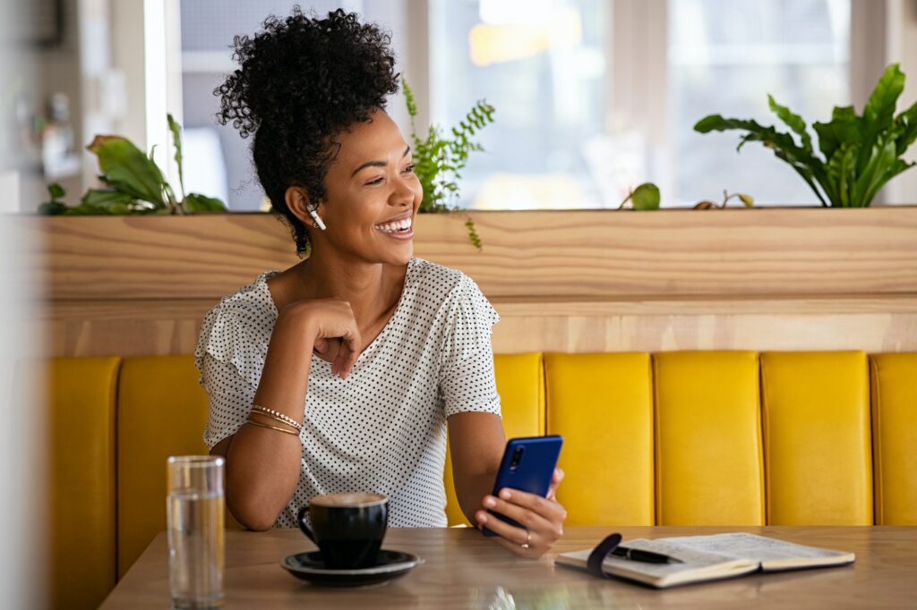 Happy woman in cafe talking on the phone with earphones