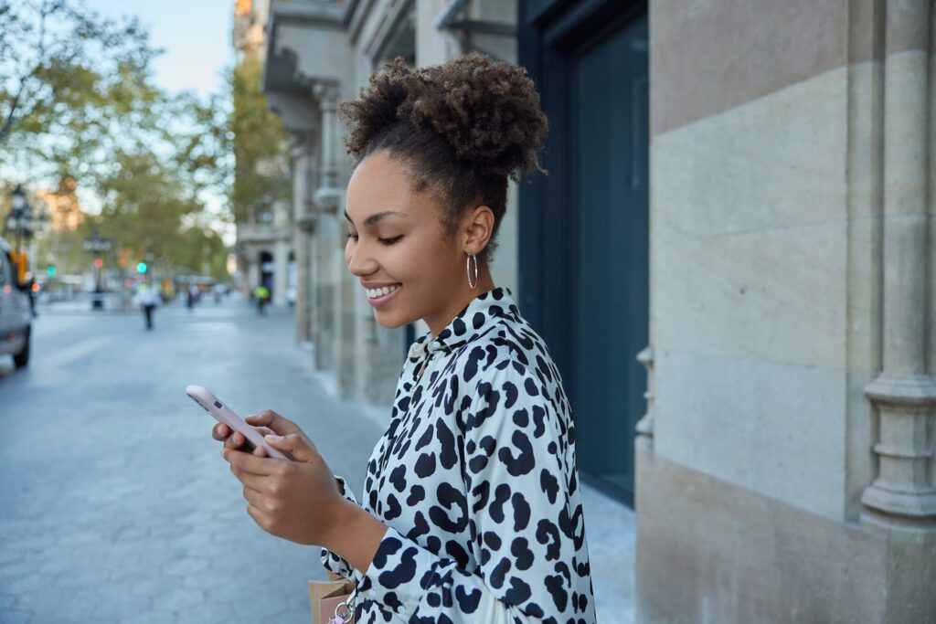 Happy carefree curly haired pretty teenager enjoys positive network messaging in social media holds